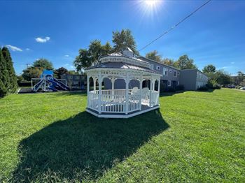 A white gazebo is situated in a grassy field with a building in the background at Townhomes at 28th, Columbus, IN, 47201